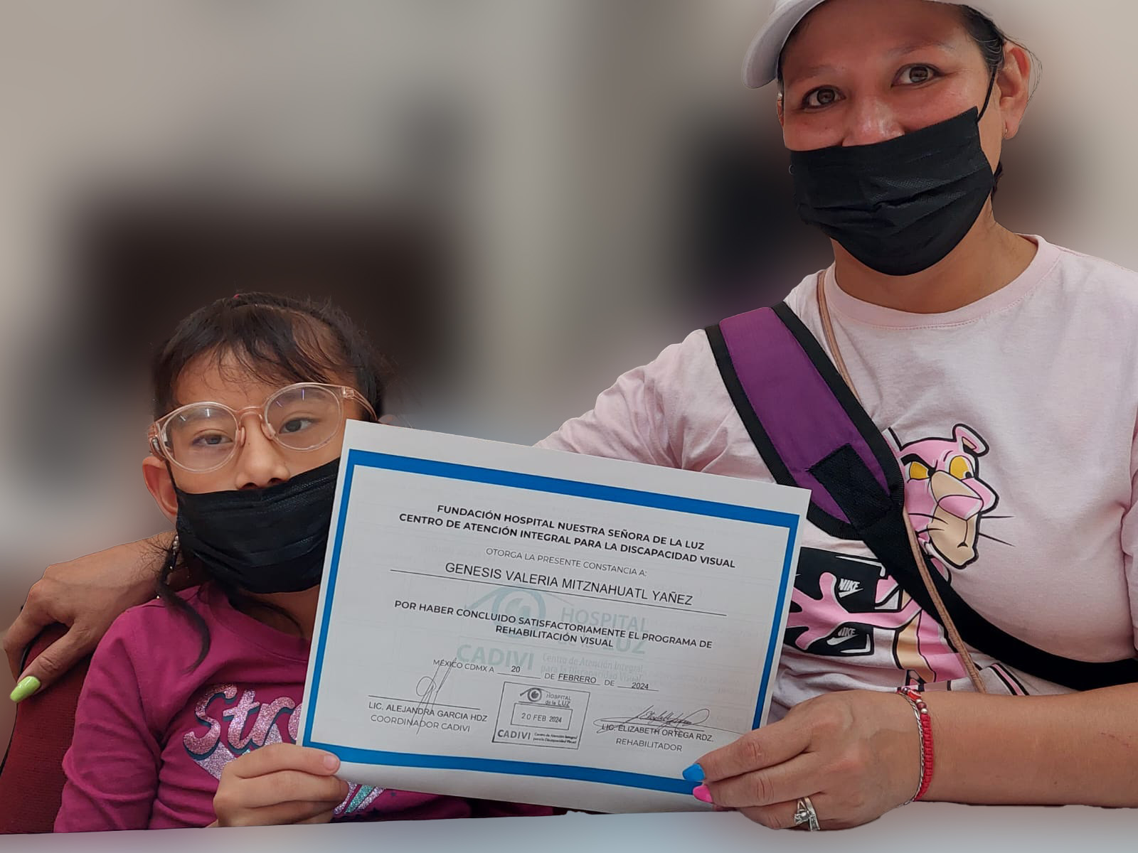 Señora con su hija sosteniendo un reconocimiento frente a la cámara