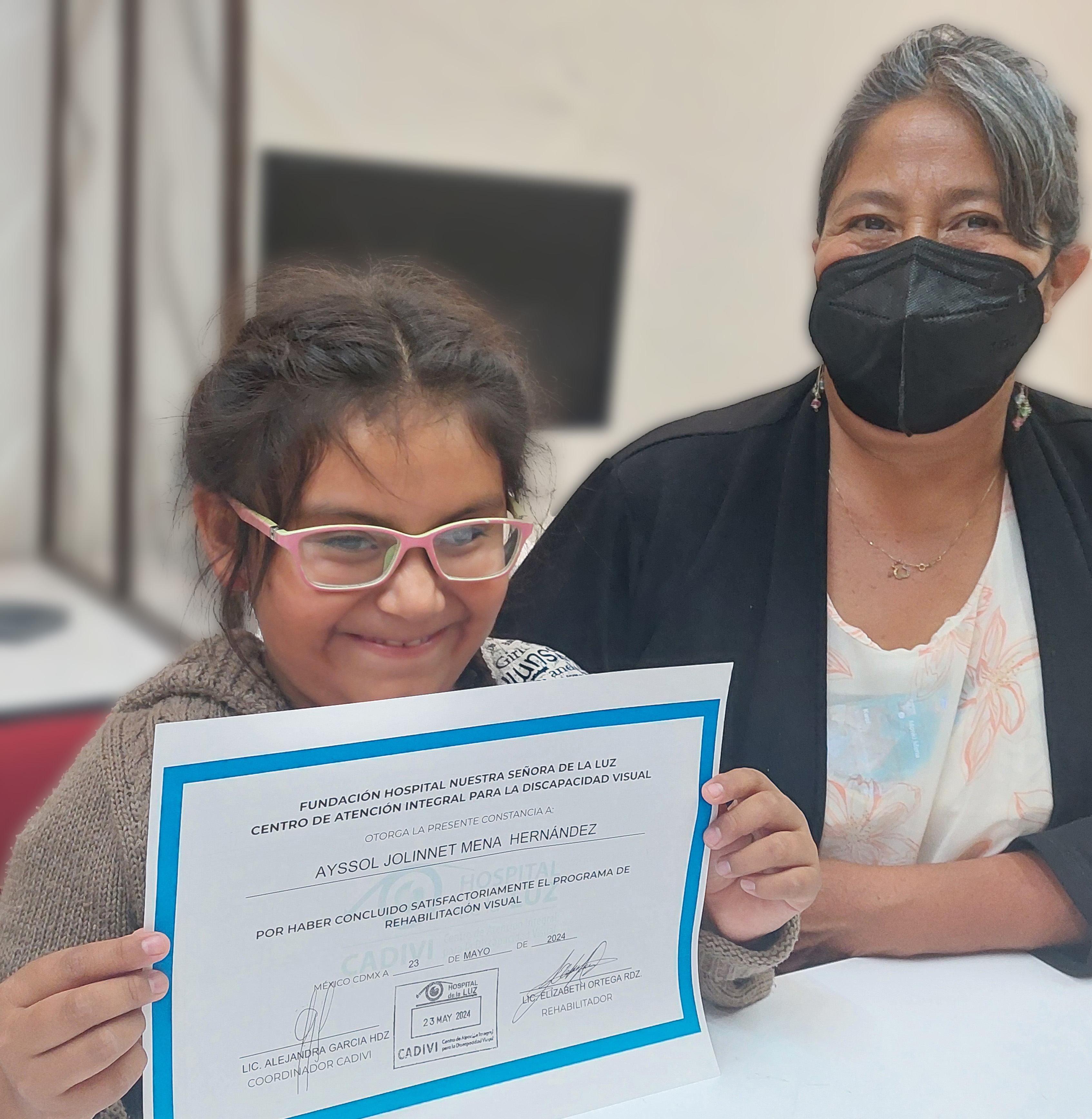 Señora con su hija sosteniendo un reconocimiento frente a la cámara