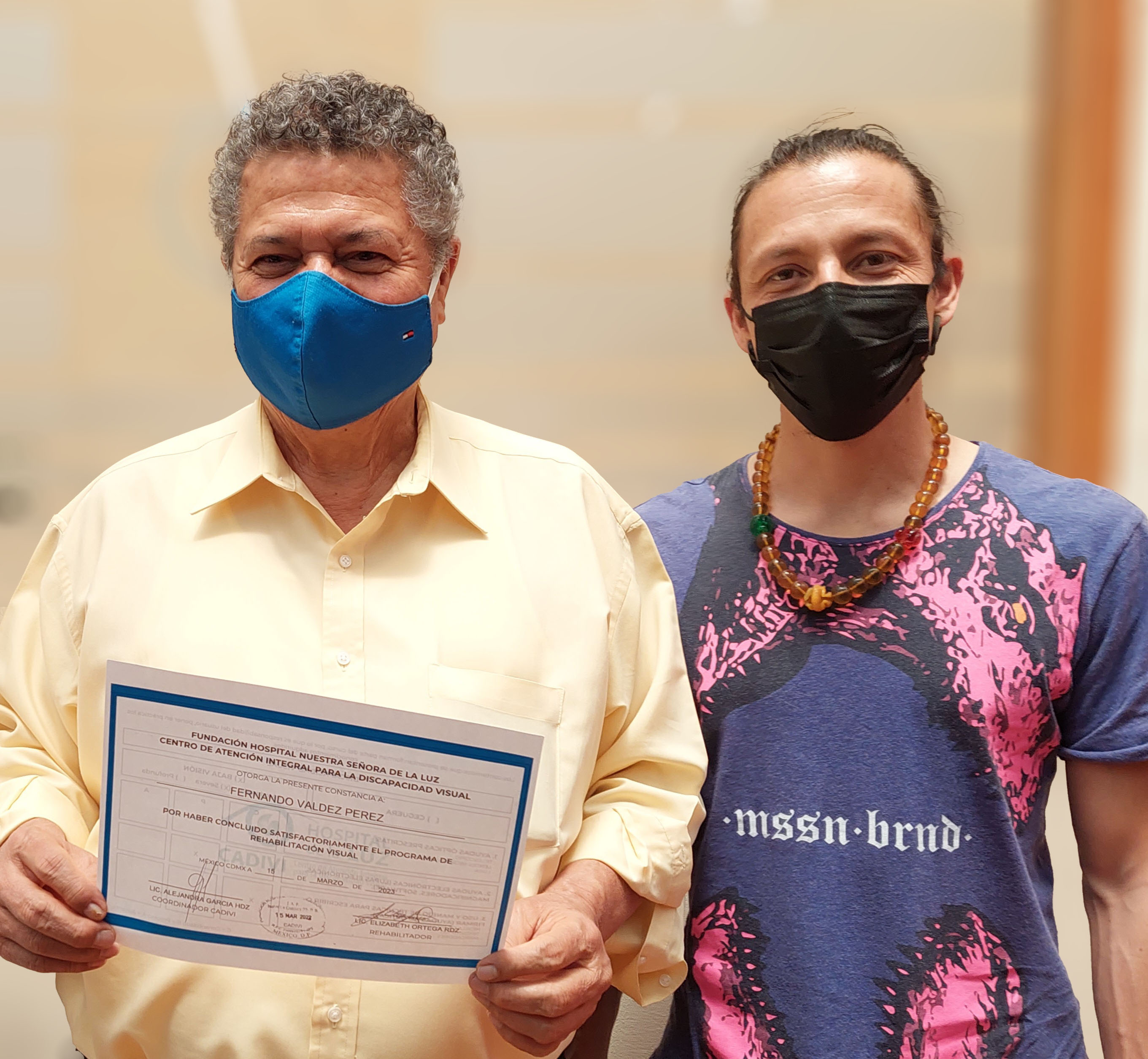 dos hombres sonriendo y el de la derecha sostiene un reconocimiento frente a la cámara